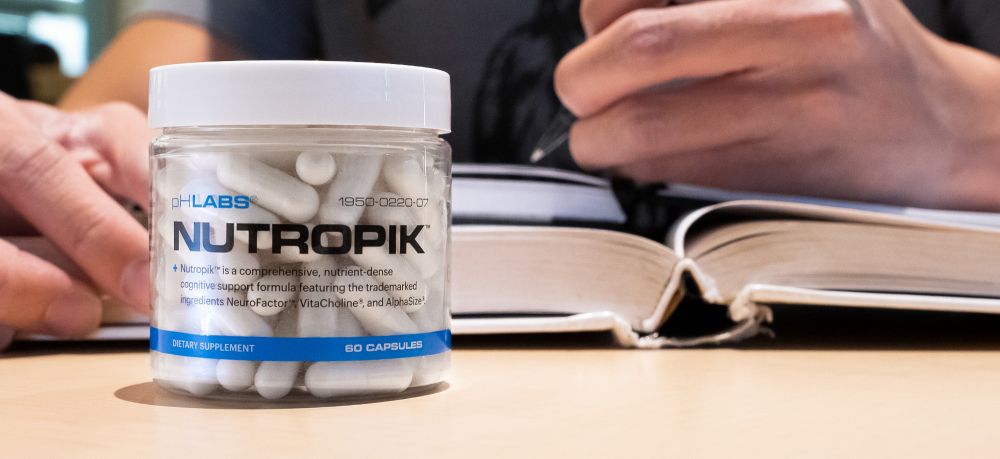 nutropik supplement bottle sitting on a table with hands and a book behind in the background