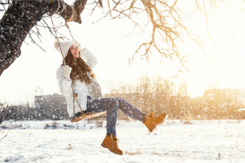 Smiling woman on a tree swing while its snowing
