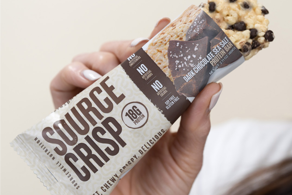 Woman holding up a Source Crisp protein bar available at NutrishopUSA.com